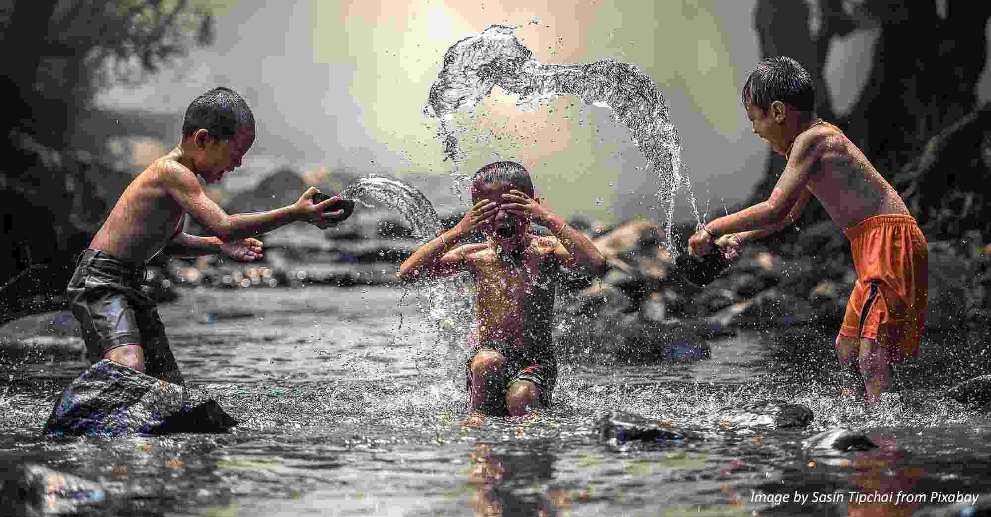 Three young boys joyfully throw water over each other playing in a river